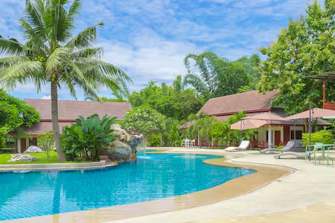Curved swimming pool surrounded by palm trees and red-roofed villas at the Chiang Dao resort