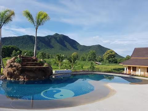 Resort pool with a yin-yang mosaic and rock waterfall against a mountain backdrop