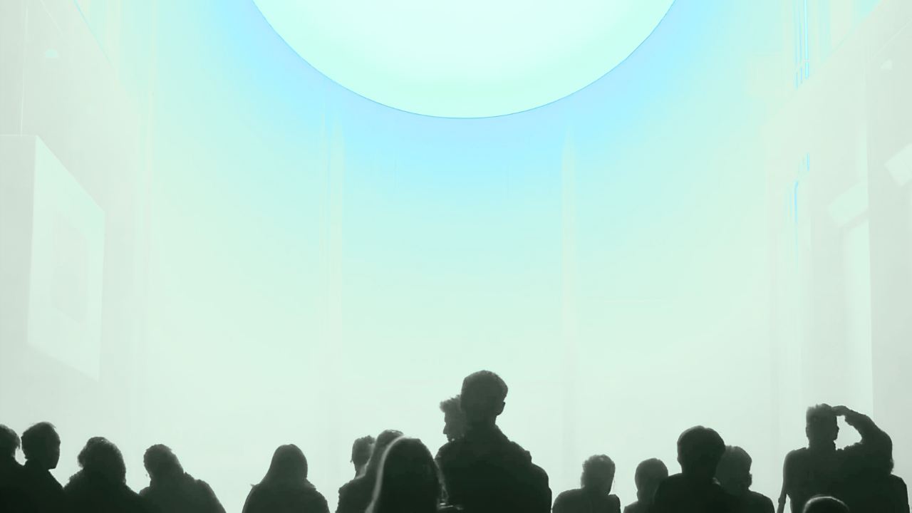 Silhouettes of people sitting together in front of a large glowing teal screen in a dark gallery space