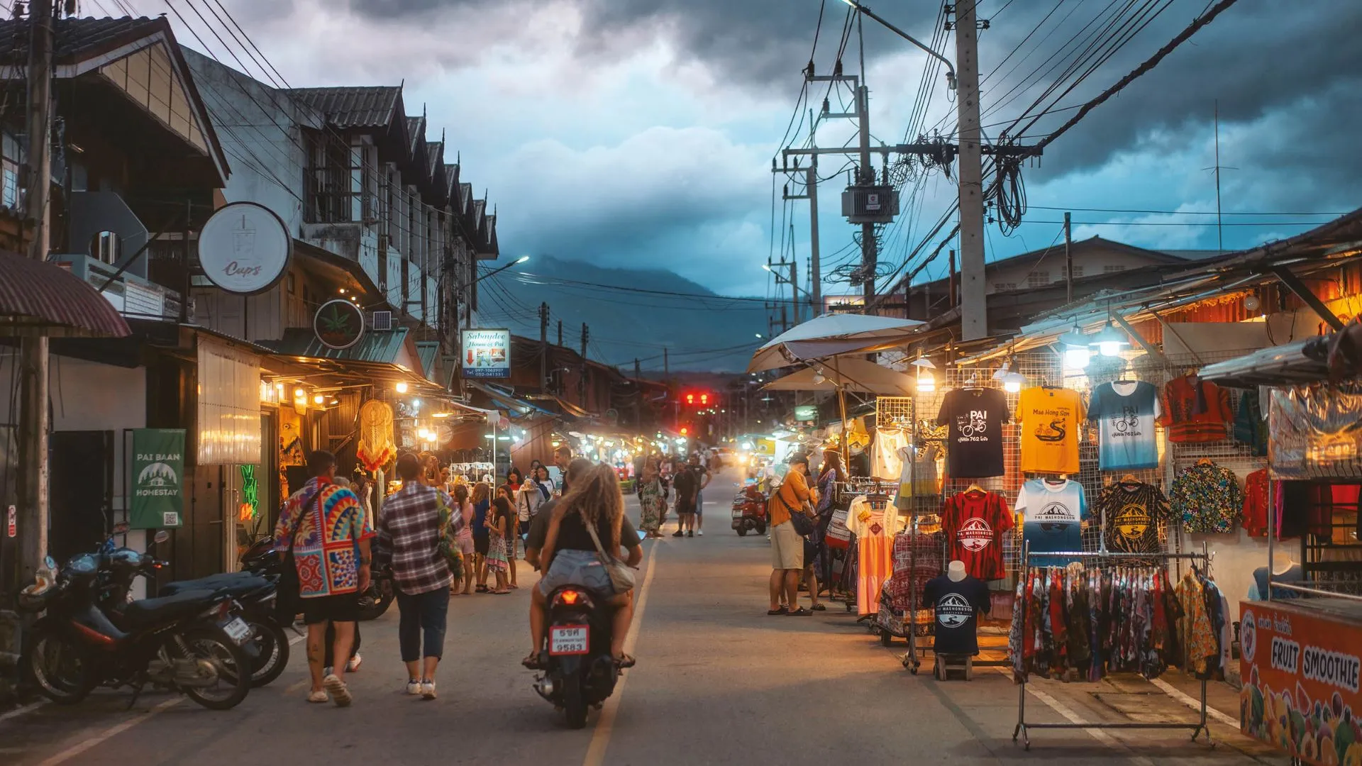 Lively evening street market in Pai, Thailand with food stalls and mountains