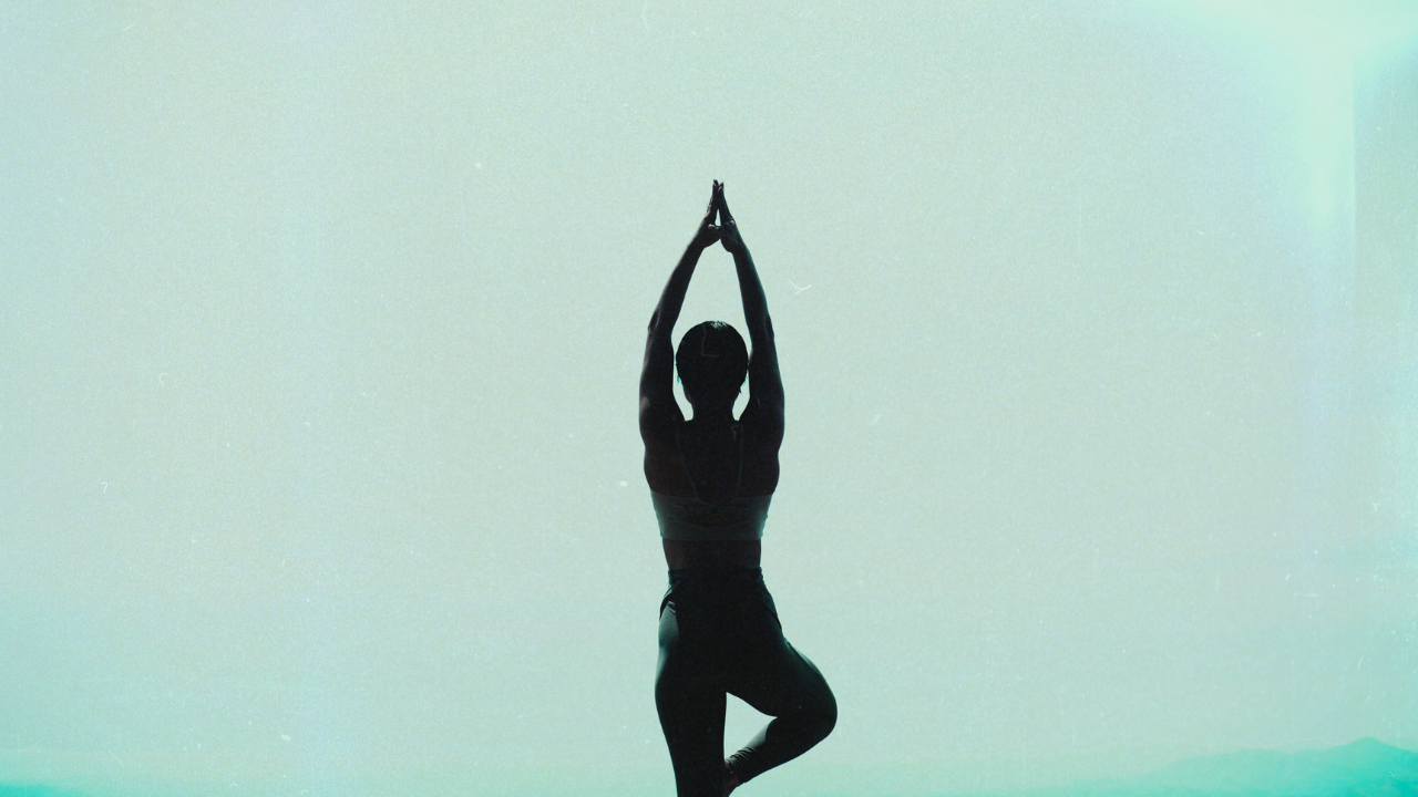 Silhouette of a person in a yoga tree pose against a soft teal background