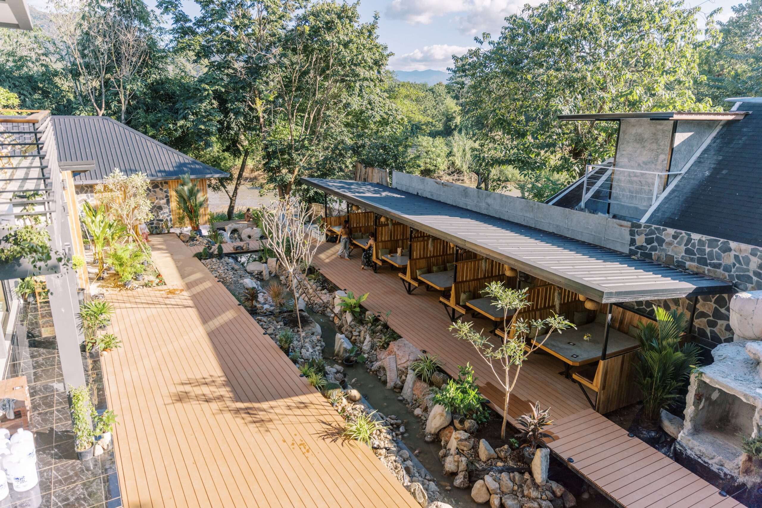 Aerial view of The Ark's wooden boardwalks along a rocky stream with riverside seating and mountains