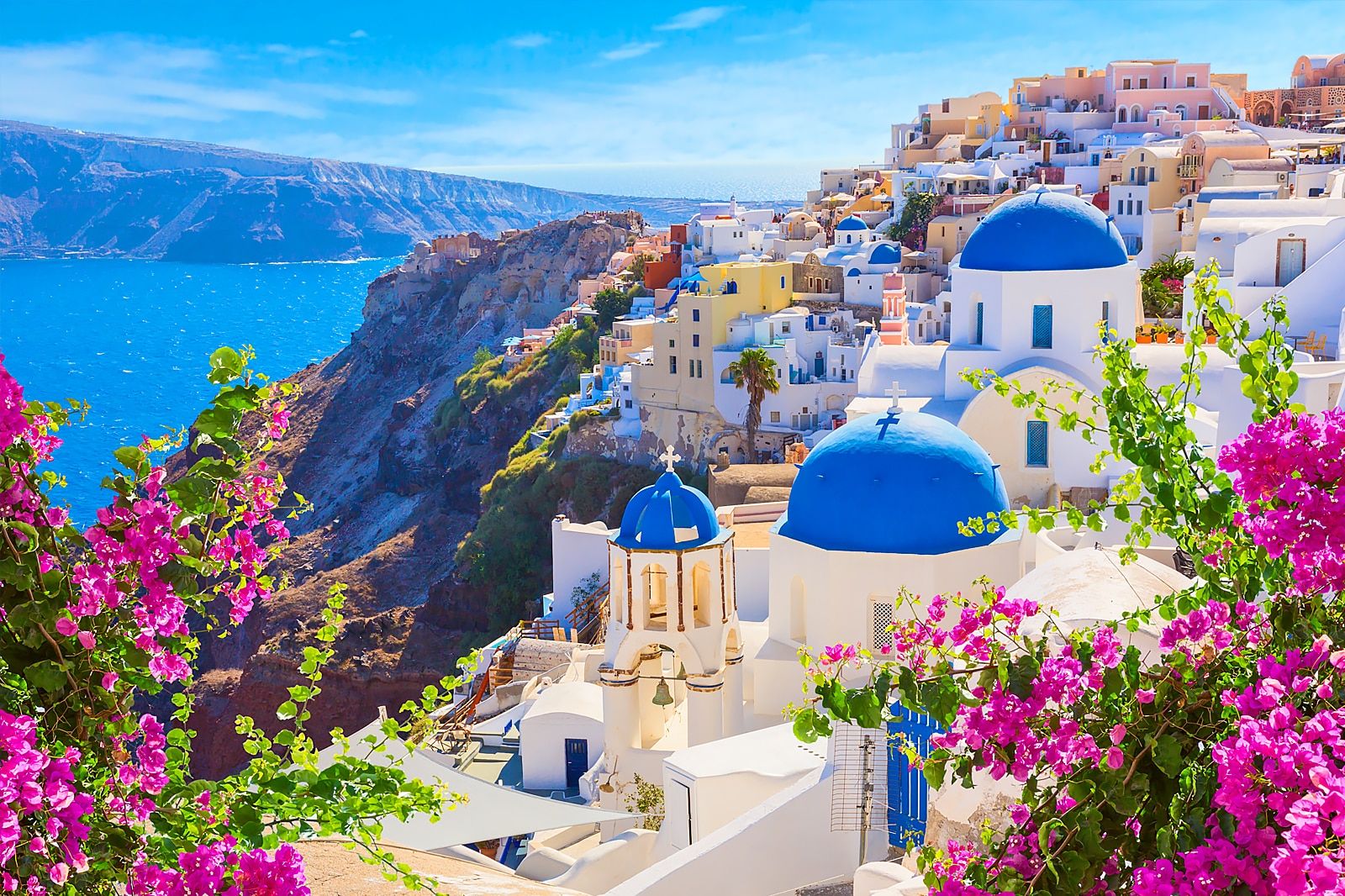 Blue-domed white churches and pink bougainvillea above the caldera in Oia, Santorini