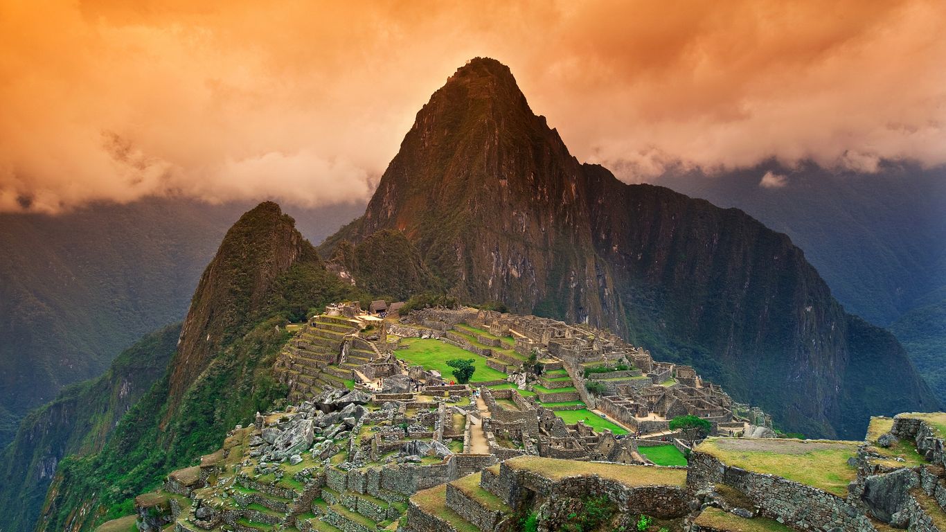 The Machu Picchu citadel beneath Huayna Picchu under an orange sunset sky