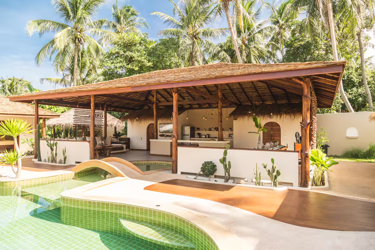 Open-air timber pavilion with a kitchen and lounge beside the pool
